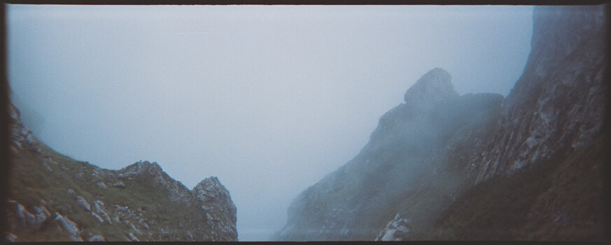 Misty mountain valley framed by steep rocky cliffs under overcast sky.