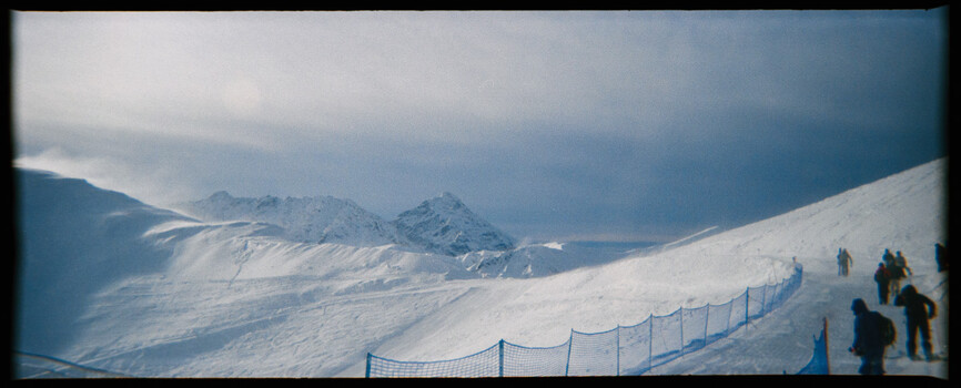 Snowy mountain slope with safety netting and scattered skiers on a ski run.