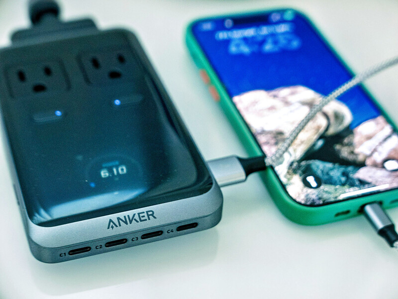 Anker portable power bank with USB-C ports connected to a green smartphone via charging cable.